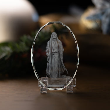 A clear crystal display stand shaped like an oval, holding a depiction of Jesus Christ referencing Matthew 14:23, set on a wooden surface with a softly blurred background.