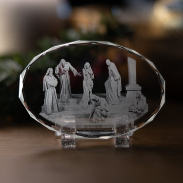 A clear faceted crystal display plaque featuring an engraved the biblical scene from John 8:1-11, where the scribes and pharasies accuse a woman of a woman of adultry, Christ states, 'He that is without sin among you, let him first cast a stone at her', shown on a small clear acrylic stand on a wooden surface with a softly blurred background.