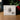The product packaging box for 'Angel Johnson Art - I Am The Light of The World' Gem V2, displayed on a wooden surface with a blurred background of green foliage and red berries.
