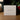 A white square product box for Angela Johnson Sculptures 'As One Who Serves V2' resting on a wooden table with a blurred background of greenery and red berries.