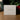 A white square product box standing on a wooden surface, printed with the signature 'Angela Johnson' and the text 'SCULPTURES INSPIRING THE LIGHT WITHIN' and 'OH MY FATHER V2'. The background is softly blurred with green foliage and red berries.