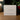 A white square product box for 'Angela Johnson Sculptures' sits on a wooden table. The box features elegant gold foil script and text reading 'Let He That Is Without Sin - Scene V2'.