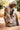 A bronze-colored statue of Jesus Christ in a kneeling, pointing pose, in Angela Johnson's work Neither Do I Condemn You, set outdoors on a stone patio with blurred trees in the background.