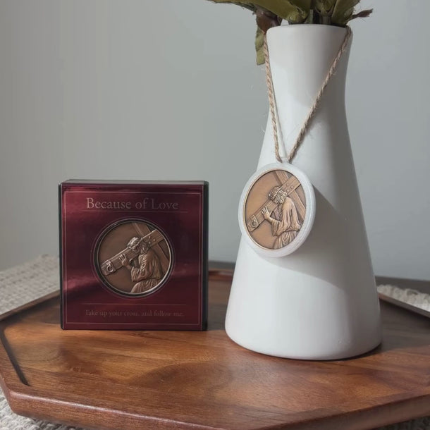 White vase with greanary, medallion pendant of Jesus Christ, based on Angela Johnson's work Because of Love, hanging from vase neck.