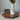 White vase with greenery and a medallion pendant hanging on then neck of the vase, based on Angela Johnson's work Neither Do I Condmen.