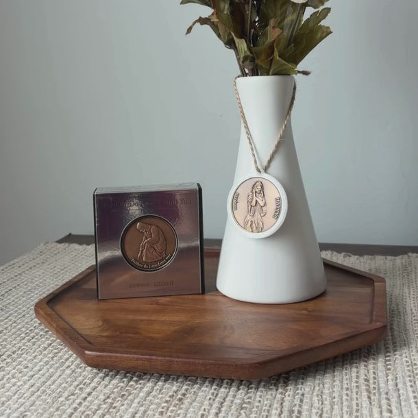 White vase with greenery and a medallion pendant hanging on then neck of the vase, based on Angela Johnson's work Neither Do I Condmen.