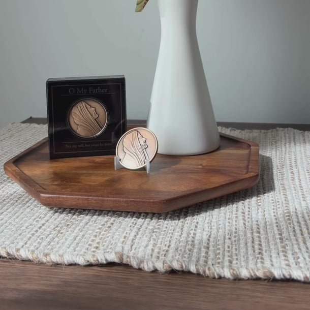 A white ceramic vase with dried green leaves in the neck, with a round bronze medallion on a clear stand featuring a profile portrait of Jesus Christ from Angela Johnson titled O My Father.